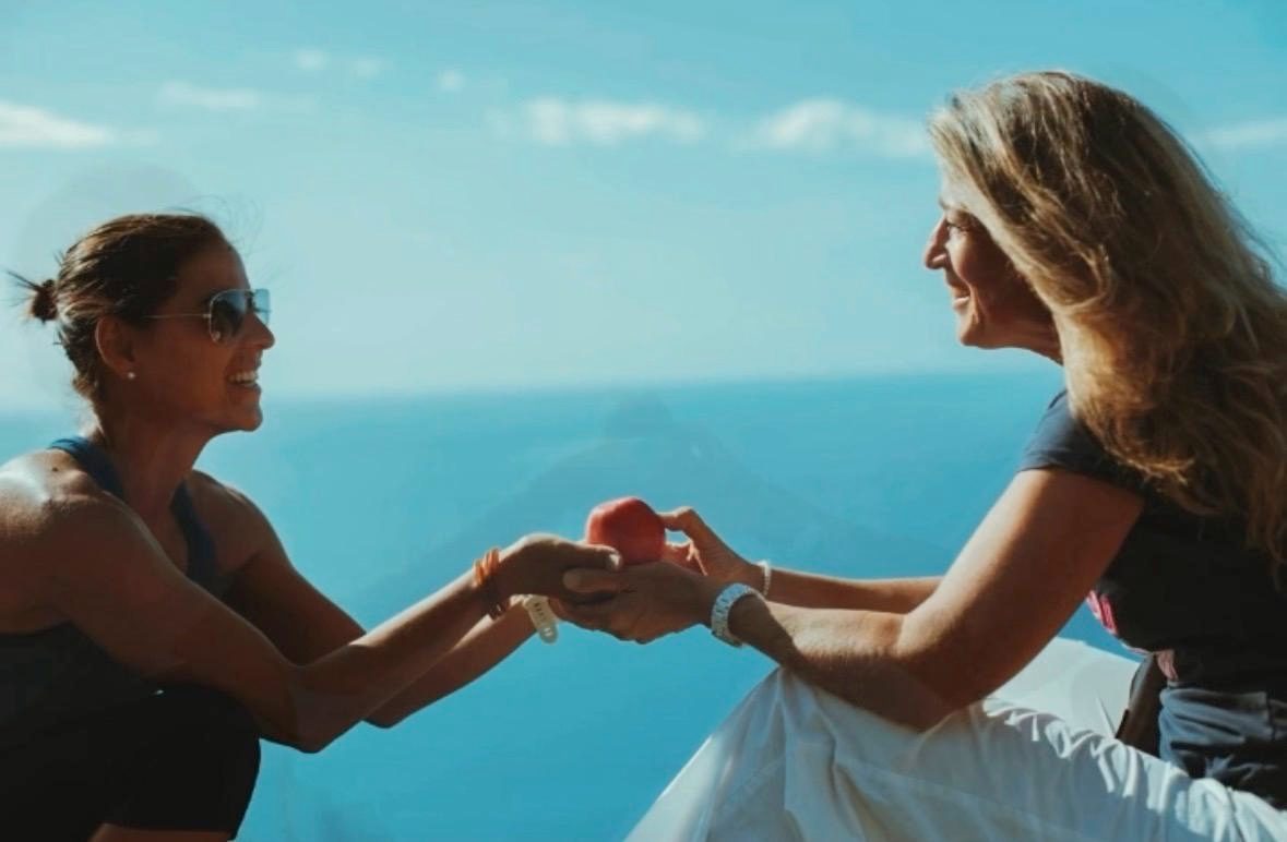 Deux femmes sur une terrasse au-dessus de la mer se tendent
                en souriant un fruit rouge &mdash; la rupture du
                je&ucirc;ne