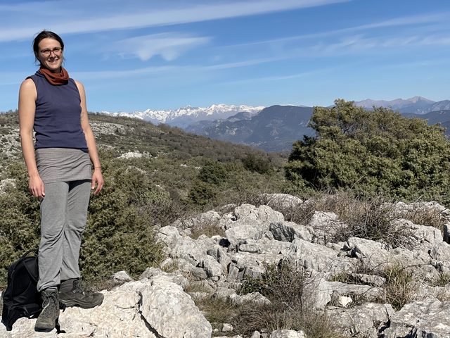 Wanderin auf einem Kalkfelsen, dahinter schneebedeckte Alpengipfel