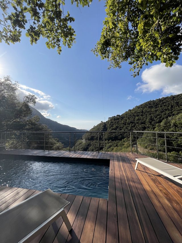 Piscine et terrasse en bois au-dessus de la vall&eacute;e, montagnes bois&eacute;es en arri&egrave;re-plan