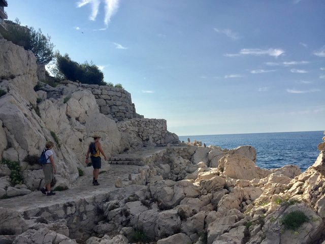 Zwei Wanderer mit Rucks&auml;cken auf einem Felsweg &uuml;ber dem Meer