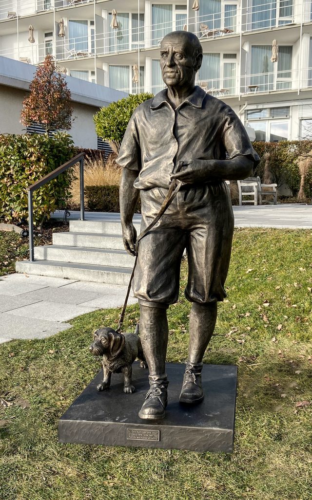 Bronzefigur von Dr. Otto Buchinger mit seinem Hund, vor einem Klinikgebäude