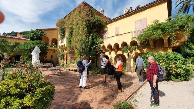Wandergruppe vor einer ockerfarbenen Villa mit Arkaden und Garten