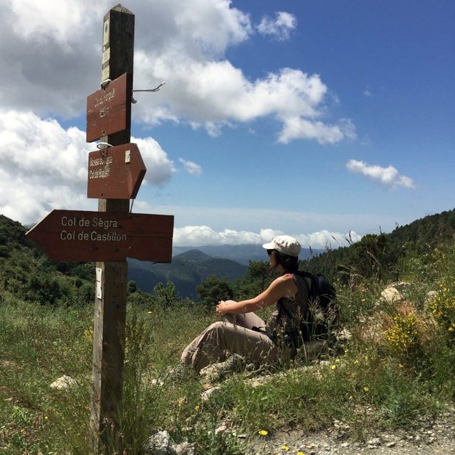 Wanderin rastet neben einem h&ouml;lzernen Wegweiser zum Col de S&eacute;gra und Col de Castillon