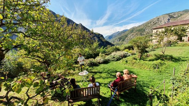 Menschen sitzen auf B&auml;nken in einer Obstwiese &uuml;ber dem Tal